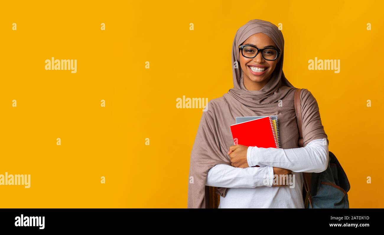 Sorridente studentessa musulmana afro in copricapo e occhiali con taccuini Foto Stock