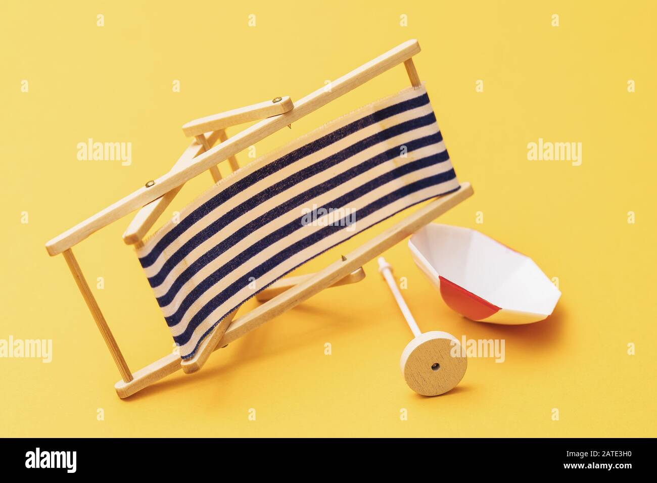 Sedia a sdraio e ombrellone cadenti su sfondo giallo. Cattivo concetto di vacanza Foto Stock