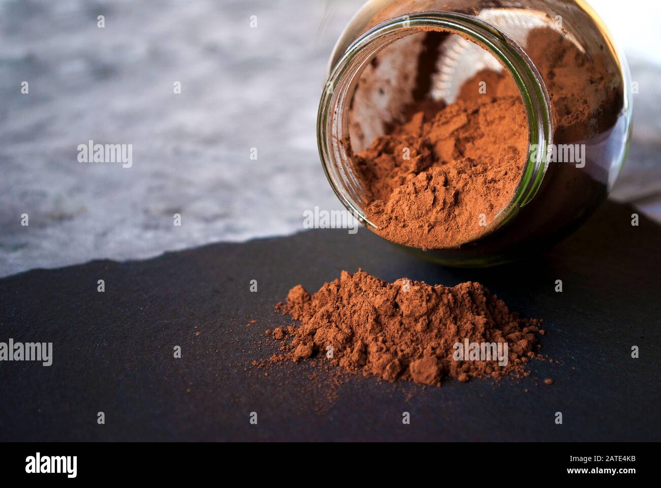 Vaso inclinato con polvere di cacao spruzzata su una tavola di pietra nera Foto Stock