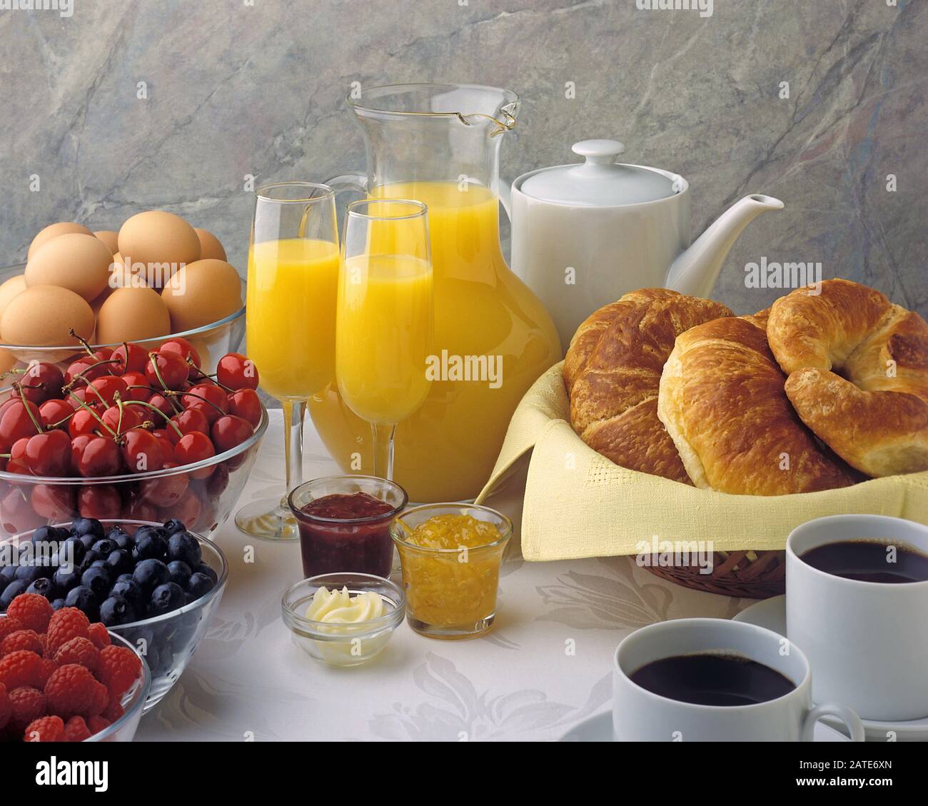 Ingredienti brunch, marmellata, marmellata, caffè, croissant, uova, ciliegie, mirtilli, lamponi, burro, succo d'arancia Foto Stock