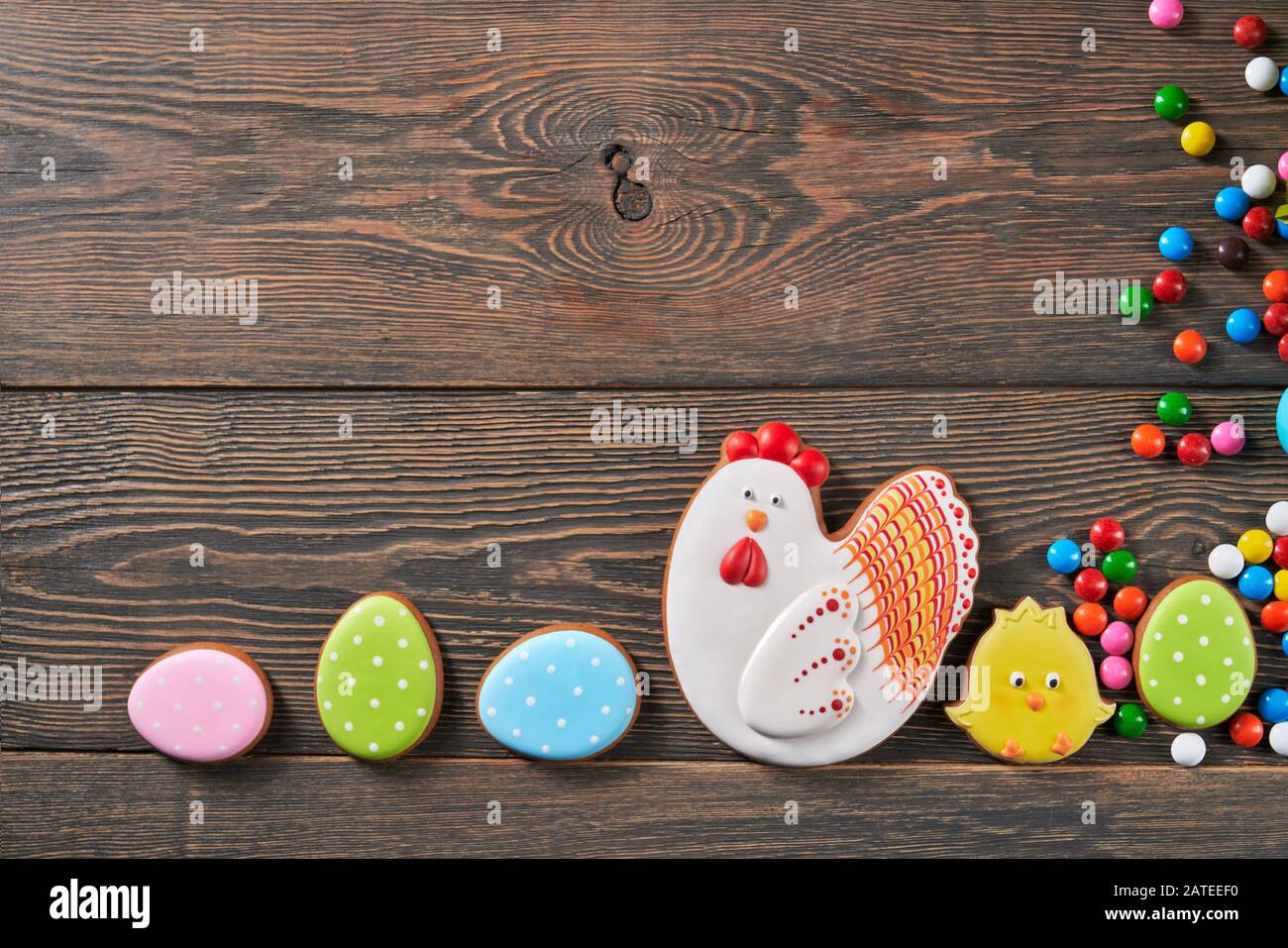 Vista dall'alto di colorati biscotti glassati allo zenzero e palline di cioccolato alle arachidi isolate su sfondo di legno. Deliziosa pasticceria fatta in casa a forma di pollo di pasqua, cazzo e uova di fila. Foto Stock