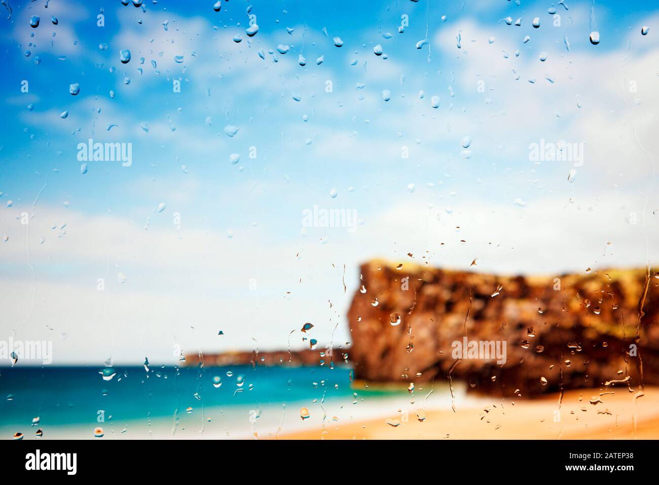 Una spiaggia dorata e scogliere viste attraverso una finestra coperta di raindrop. Foto Stock