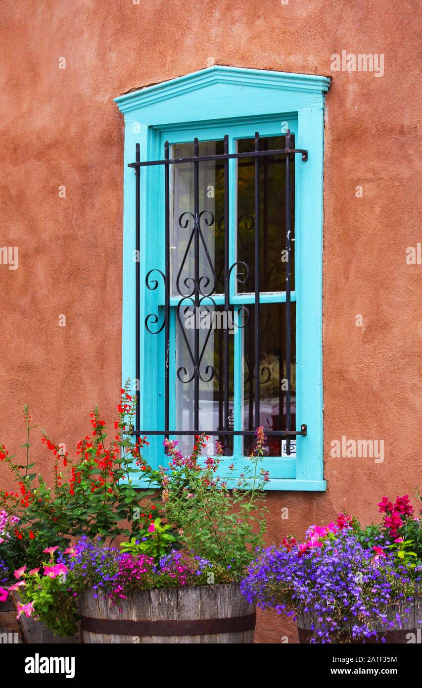 Finestra in legno di legno blu nell'edificio in gesso di adobe con fiori colorati e luminosi. Griglie in metallo decorate sulla finestra. Santa Fe, New Mexico, Sud-Ovest Foto Stock