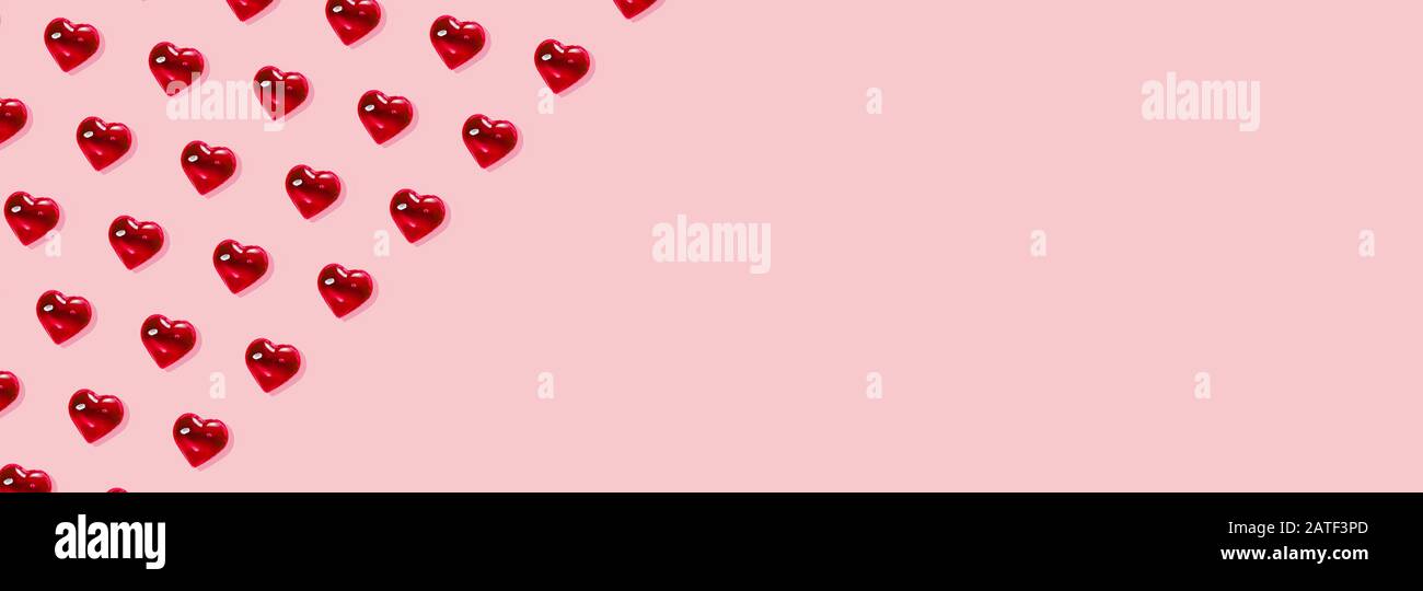 San Valentino sfondo. Motivo di cuori rossi di vetro su sfondo rosa pastello. Minimalismo della carta, simbolo dell'amore. Foto Stock