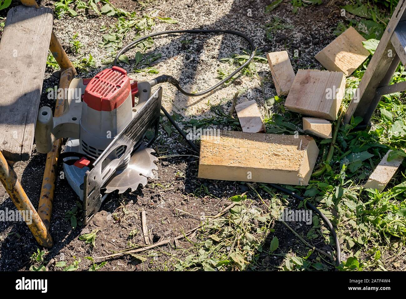 una sega circolare manuale elettrica si trova a terra vicino agli scarti di tavole di legno, non conforme alle norme di sicurezza Foto Stock