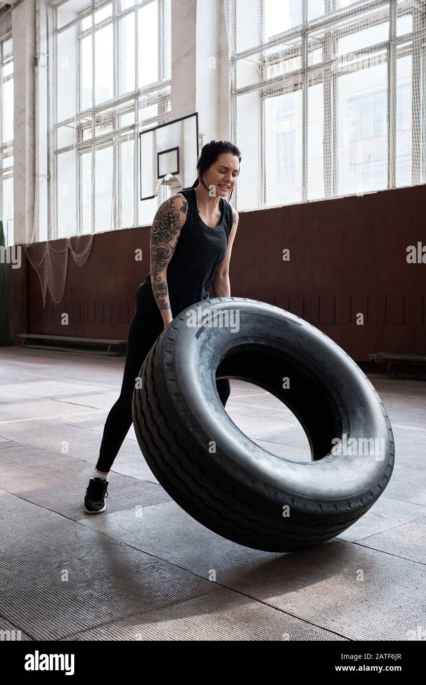 Atletica tatuata caucasica donna in nero sportswear flipping pneumatico pesante Foto Stock