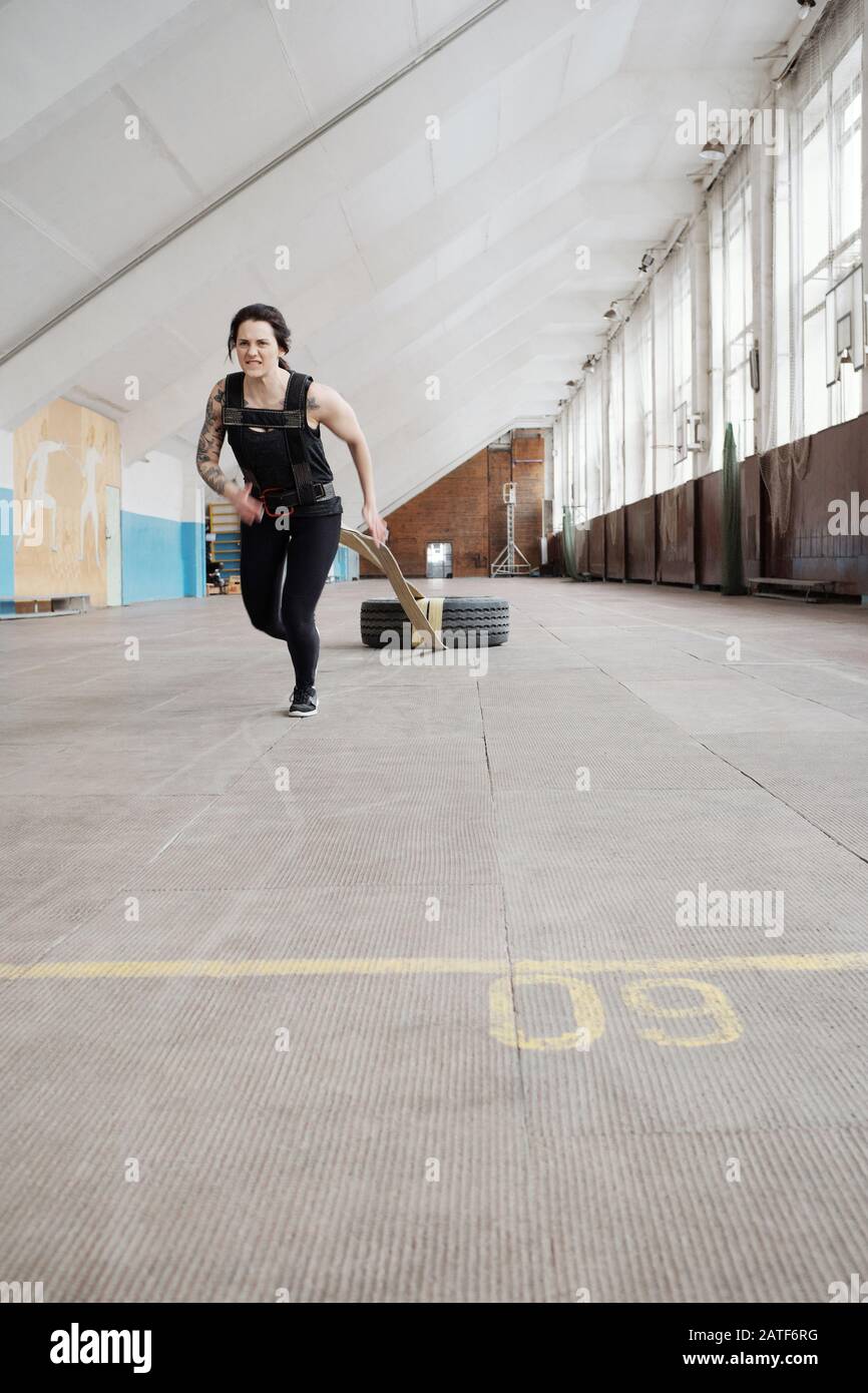 Determinata donna atletica in nero sportswear correre e trascinare pneumatico Foto Stock
