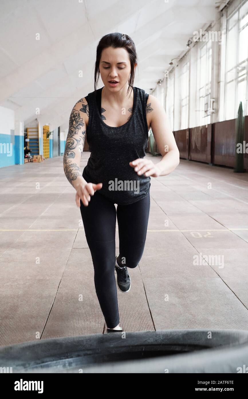 Donna caucasica ottenere pneumatico per fare esercizi di cross training in palestra Foto Stock