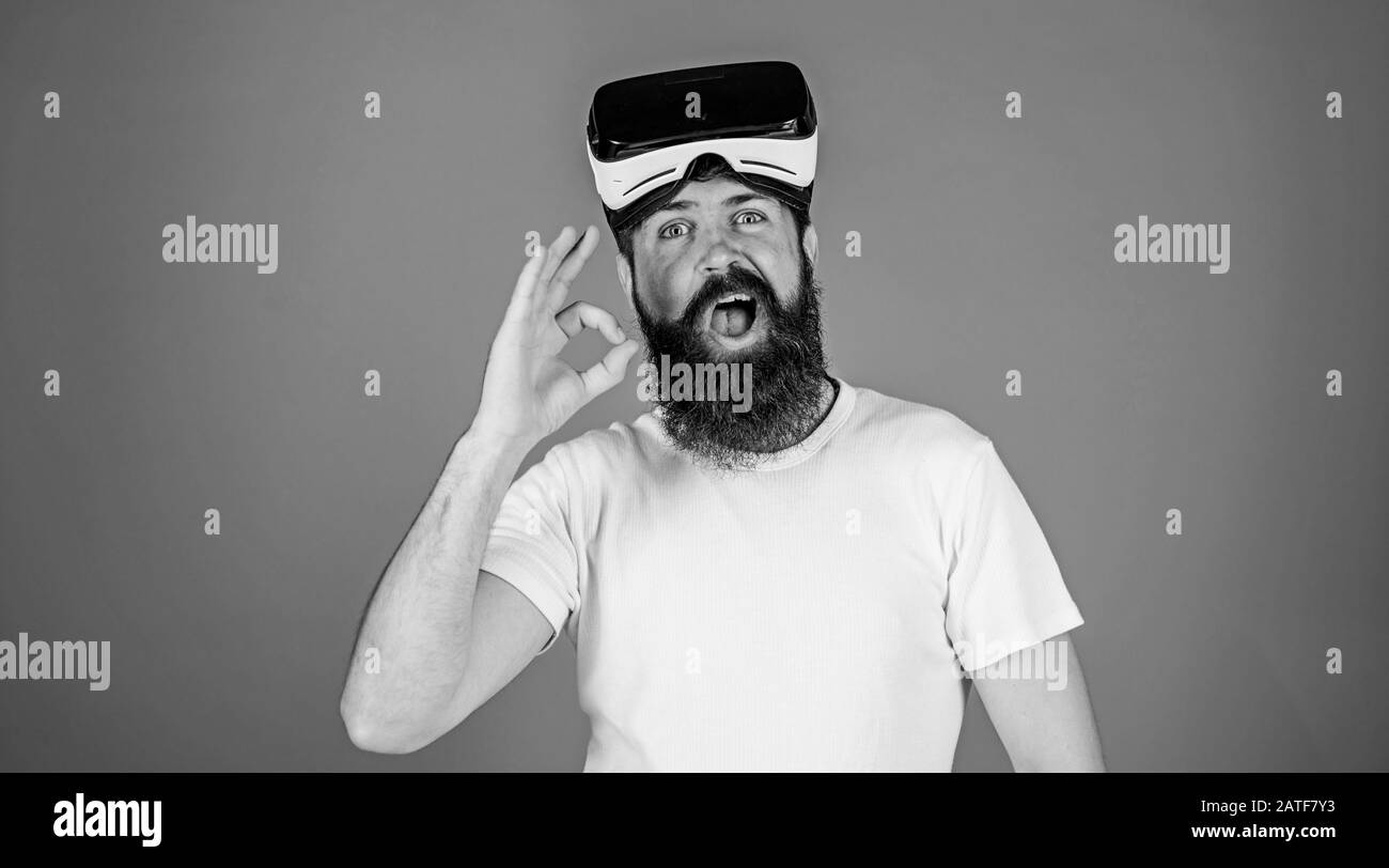 Uomo con barba lunga e viso divertente che mostra il gesto OK. Hippster con la barba alla moda che indossa occhiali VR, concetto di tecnologie digitali. Bearded man test 3D video plugin isolato su sfondo blu. Foto Stock