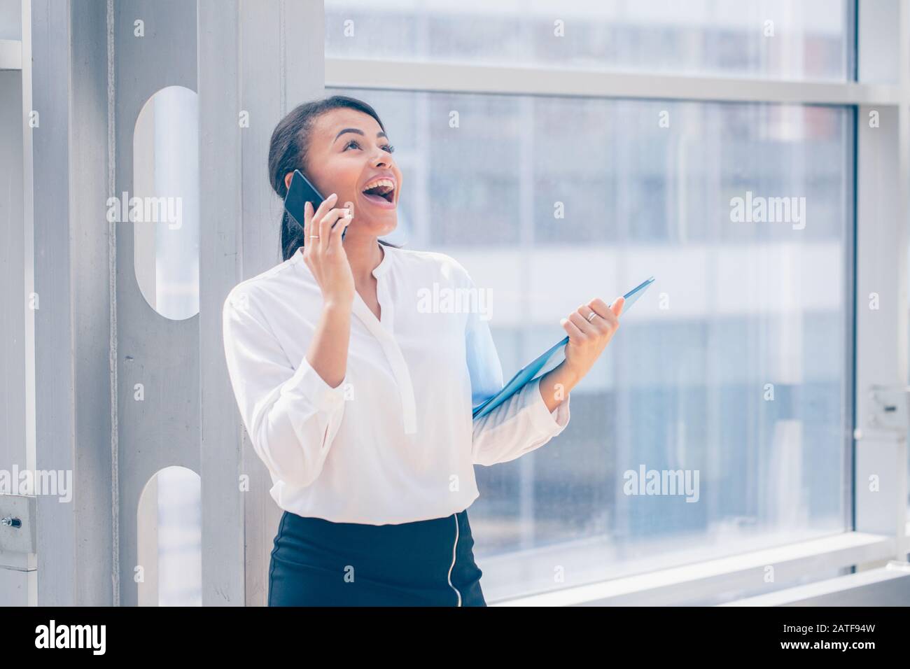Felice imprenditrice africana sorridente e parlare al telefono tenendo una cartella di documenti Foto Stock