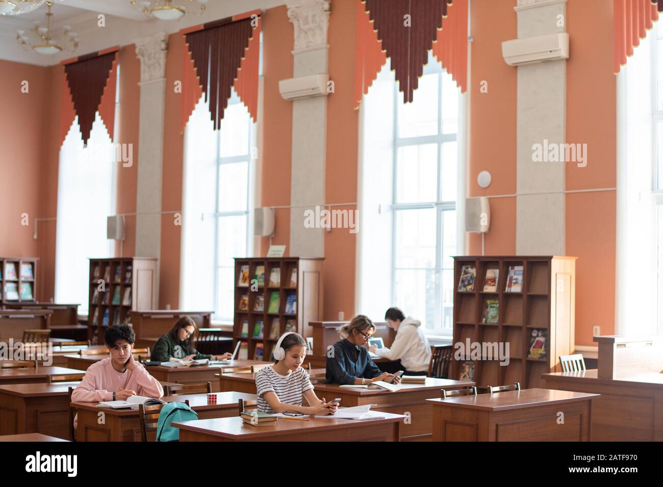 Due file di scrivanie nella biblioteca universitaria e studenti che lavorano individualmente Foto Stock