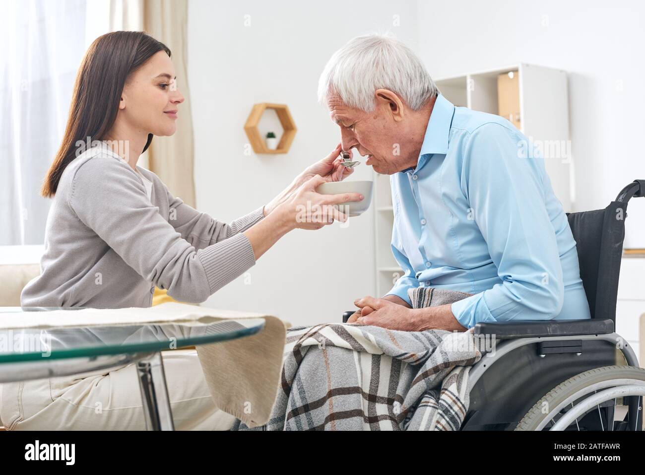 Assistente sociale che tiene la ciotola con la minestra ed il cucchiaio dalla bocca dell'uomo anziano disabile Foto Stock
