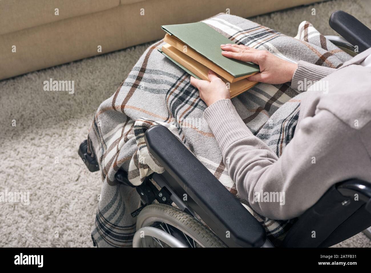 Mani di giovane disable donna in sedia a rotelle che tiene libro sulle sue ginocchia Foto Stock