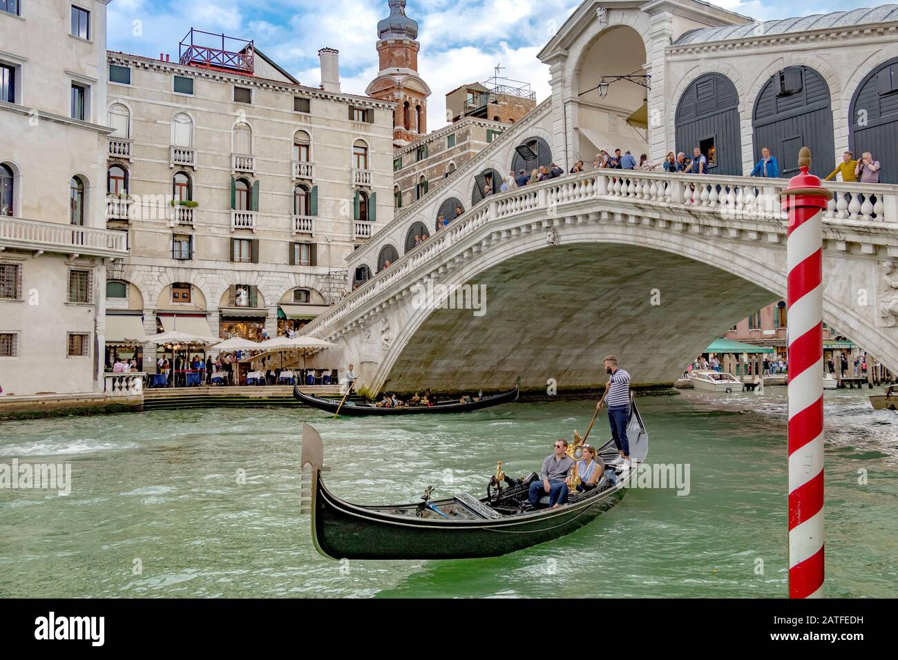 Una gondola con due persone che fa un giro in gondola davanti al Ponte di Rialto, il più antico dei quattro ponti che attraversano il Canal Grande di Venezia Foto Stock