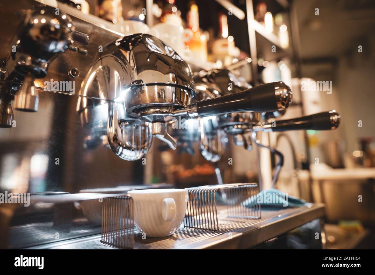 Immagine a bassa profondità di campo (messa a fuoco selettiva) con una tazza professionale di caffè metallico e macchina per caffè espresso in una caffetteria. Foto Stock