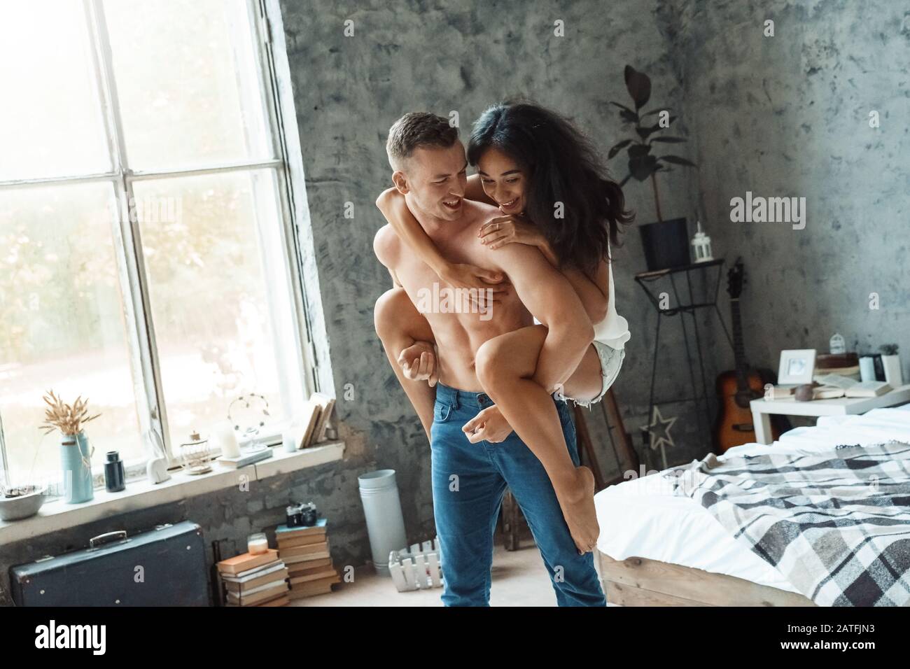 Coppia Mista Race. Giovane uomo che porta la donna in camera da letto ridendo gioioso Foto Stock