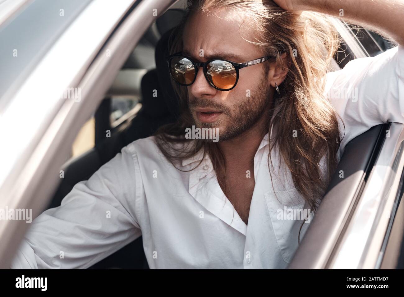 Giovane adulto seduto in auto con occhiali da sole Foto Stock