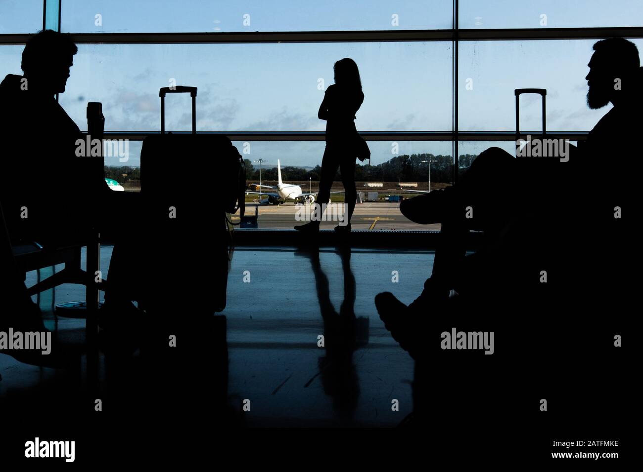 Sagoma dei passeggeri delle compagnie aeree in una sala d'aeroporto all'ampia finestra di osservazione che guarda un aereo che vola contro un tramonto surreale. Dublino Foto Stock