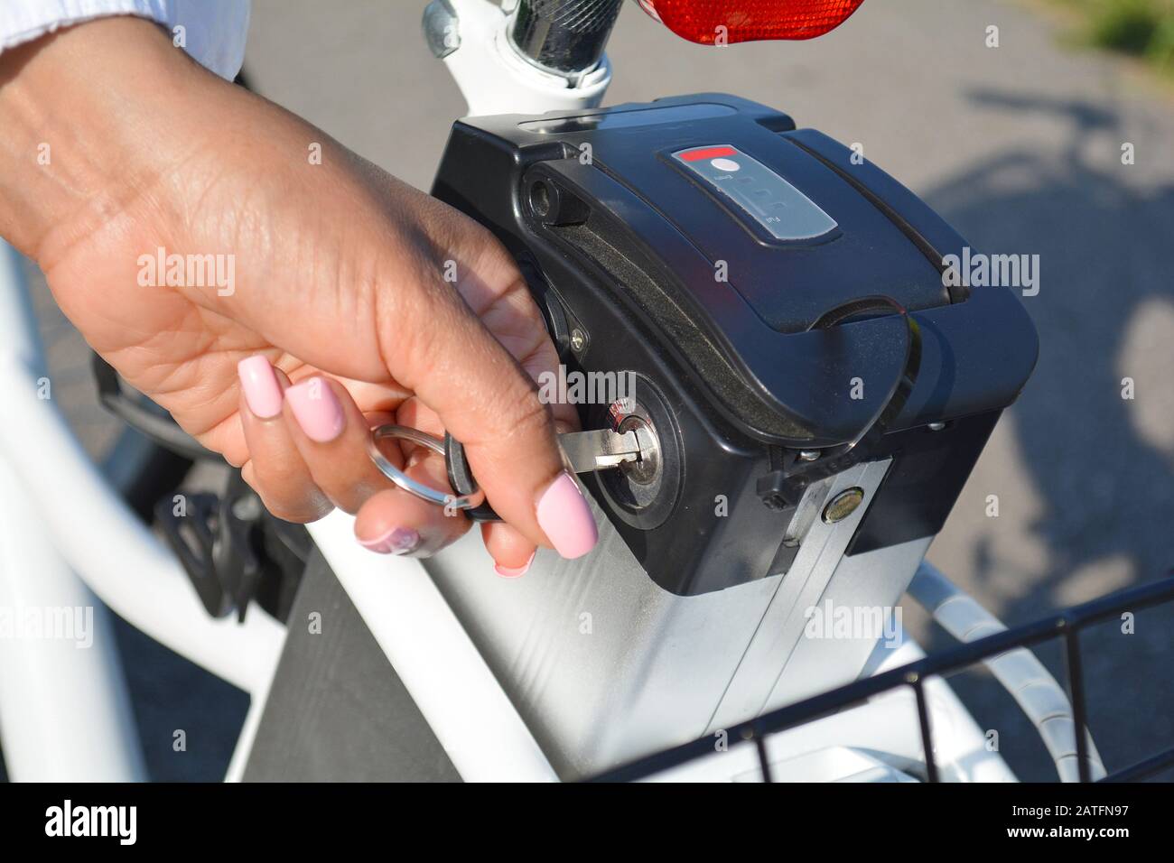 Donne ciclista tenere premuto il tasto della bicicletta elettrica batteria. Interruttore femmina alimentato e moto con la chiave in posizione di park nella soleggiata giornata estiva. Close up Foto Stock