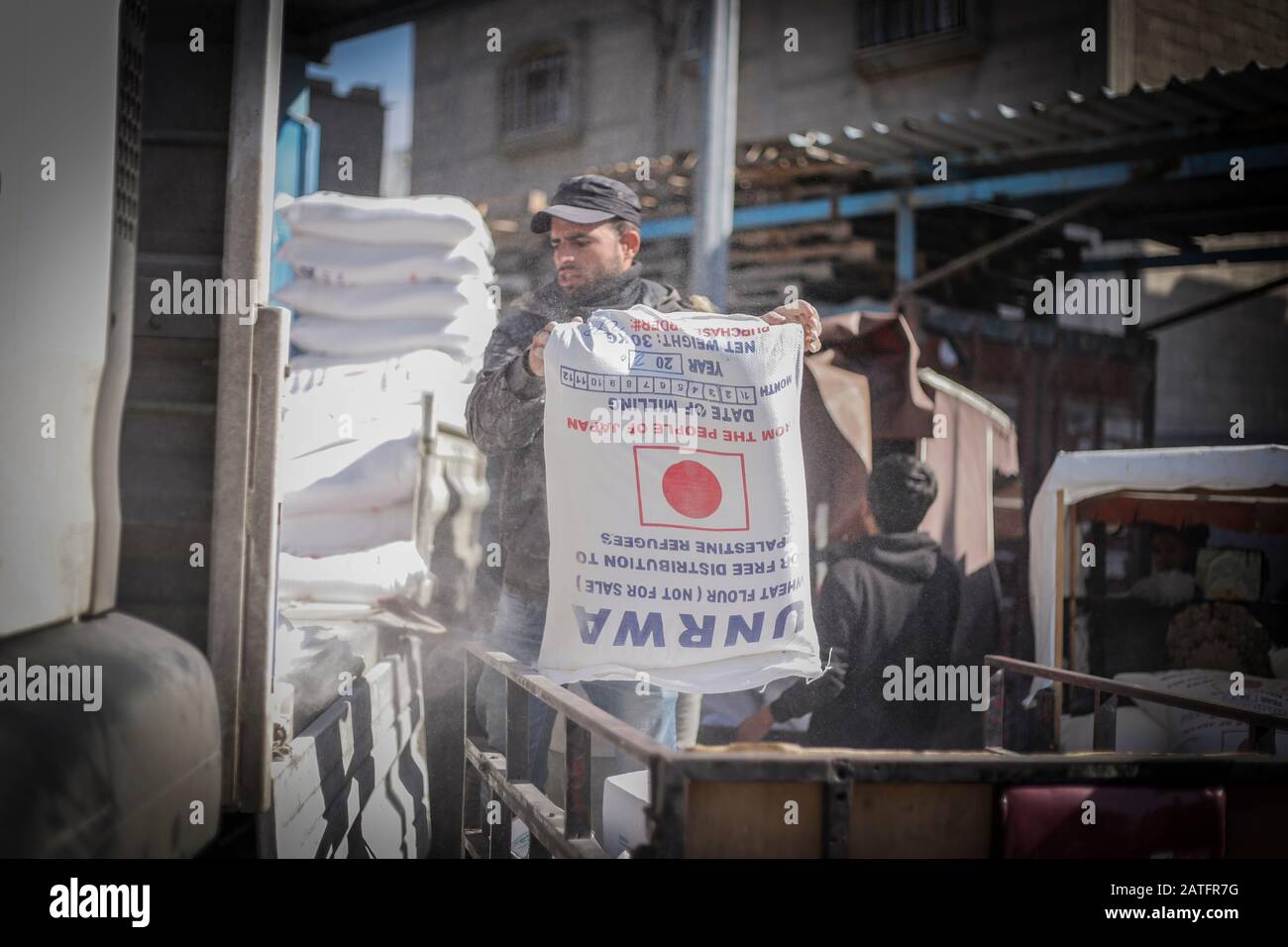 Un uomo porta un sacco di farina parte dell'aiuto alimentare dell'Agenzia delle Nazioni Unite per il soccorso e l'occupazione (UNRWA) in un centro di distribuzione nel campo di Khan Yunis per i rifugiati palestinesi nella striscia meridionale di Gaza. Foto Stock