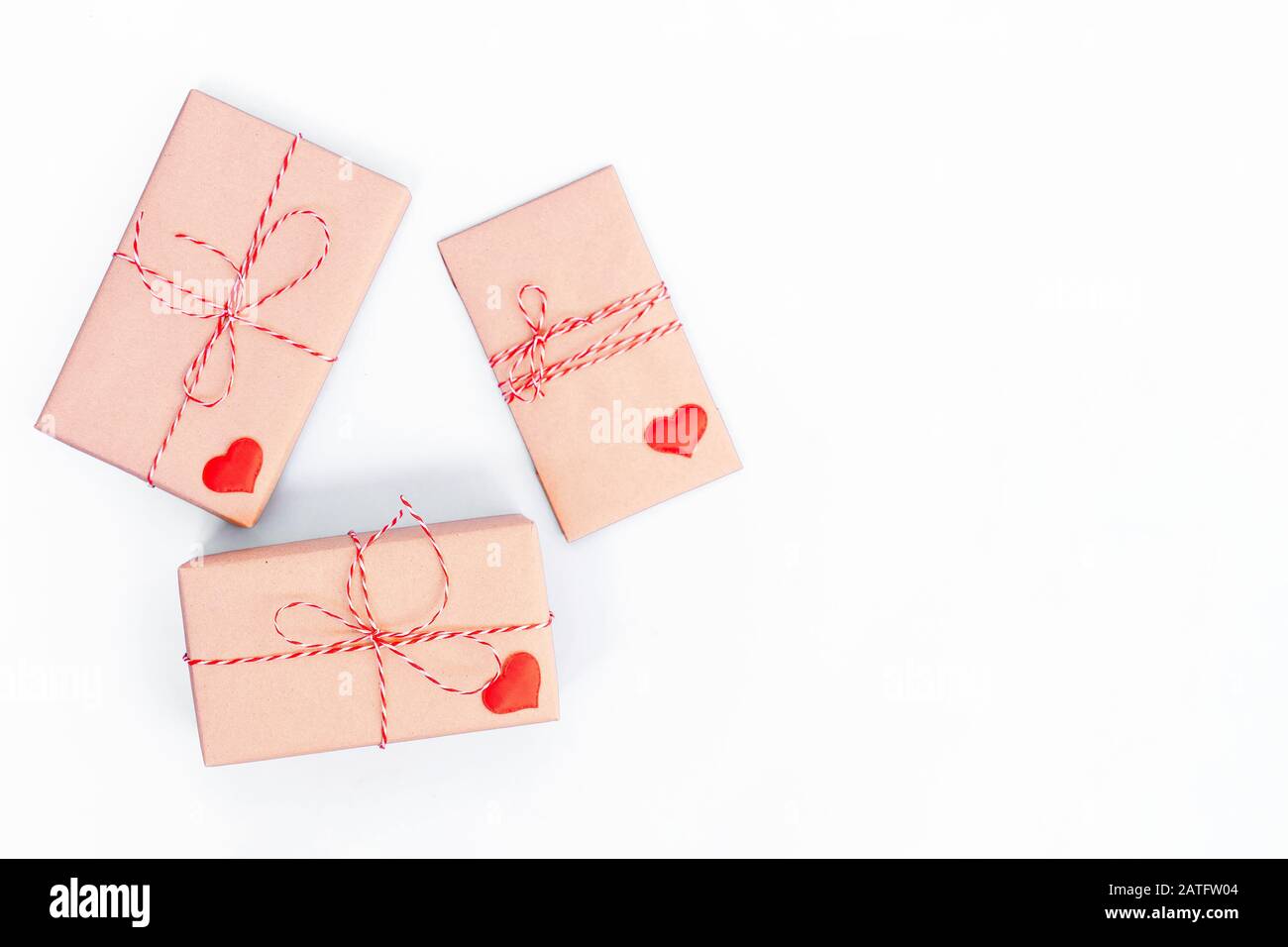 Scatole regalo avvolte in carta artigianale e decorate con nastro rosso e cuori di legno su sfondo bianco. Giorno di San Valentino, matrimonio o altre decorazioni di vacanza sfondo Foto Stock