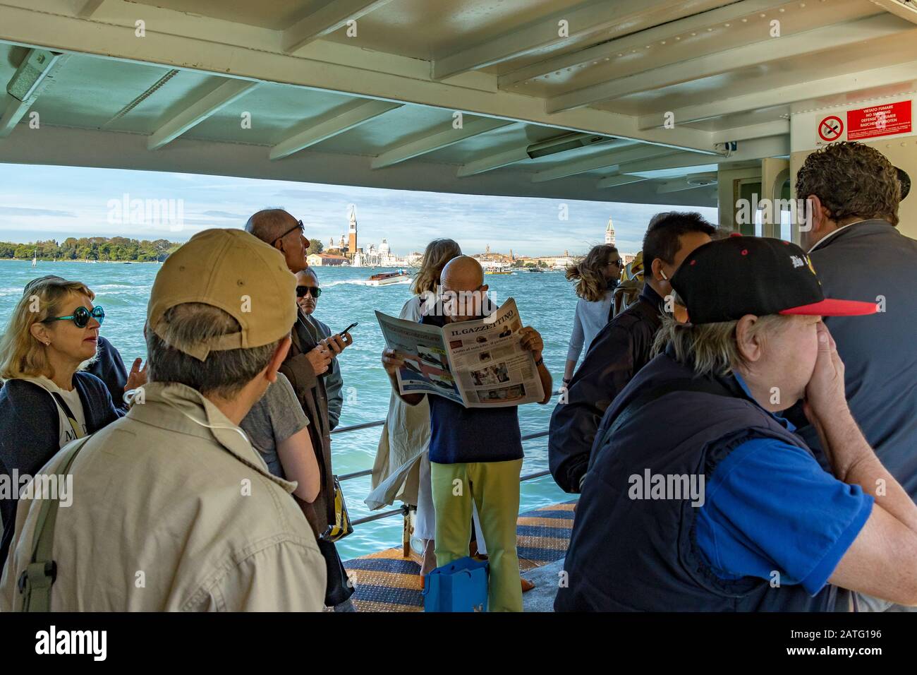 Un uomo che legge un giornale vicino ad altri passeggeri su un Vaporetto o servizio di vaporetto sulla Laguna di Venezia, sulla rotta per Venezia, Italia Foto Stock