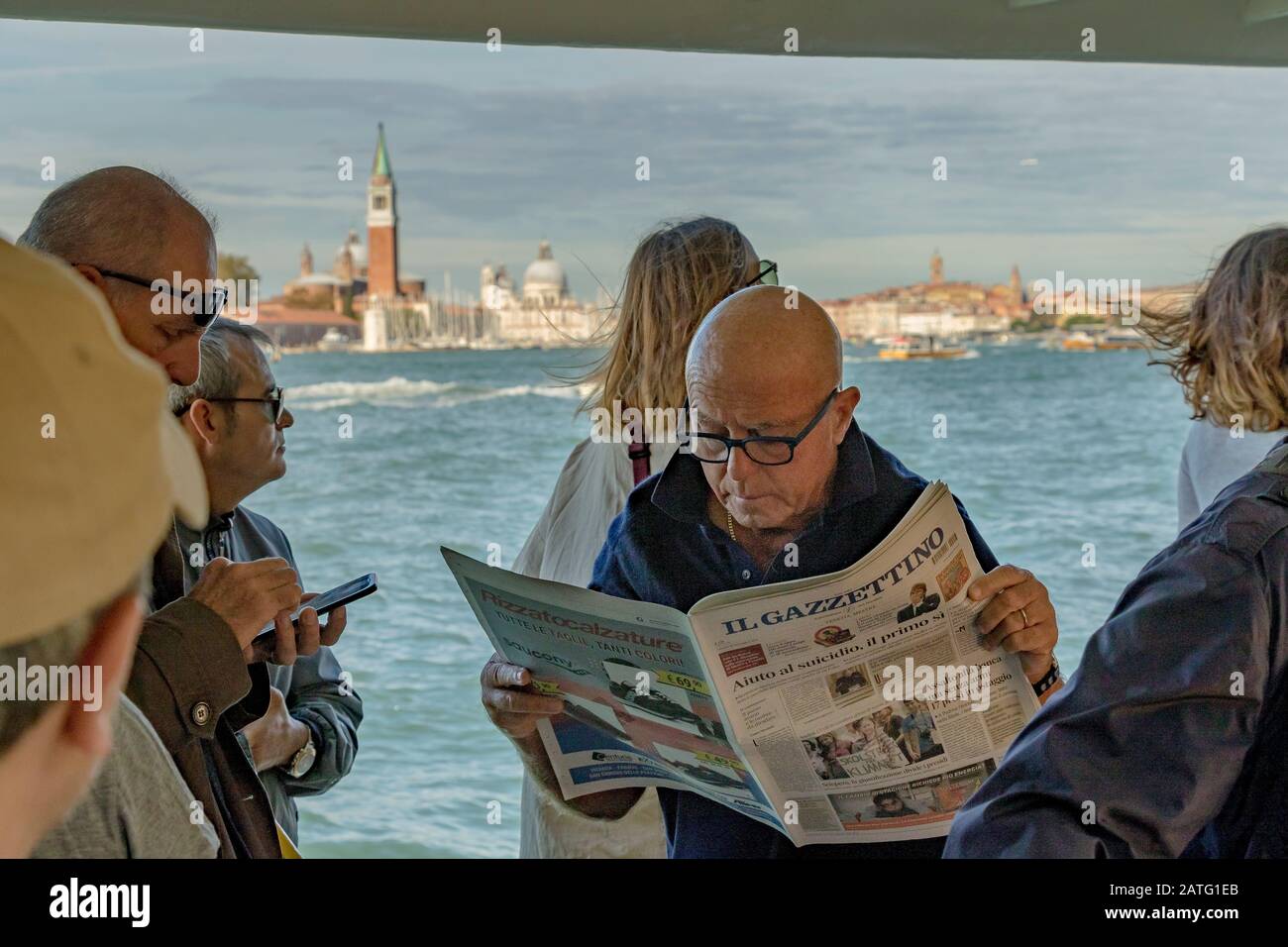 Un uomo che legge un giornale vicino ad altri passeggeri su un Vaporetto o servizio di vaporetto sulla Laguna di Venezia, sulla rotta per Venezia, Italia Foto Stock