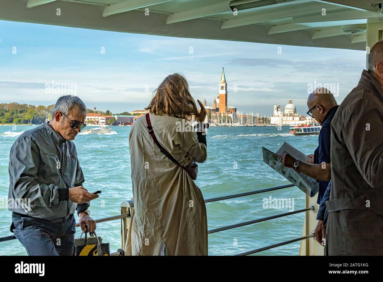 Un uomo che legge un giornale vicino ad altri passeggeri su un Vaporetto o servizio di vaporetto sulla Laguna di Venezia, sulla rotta per Venezia, Italia Foto Stock