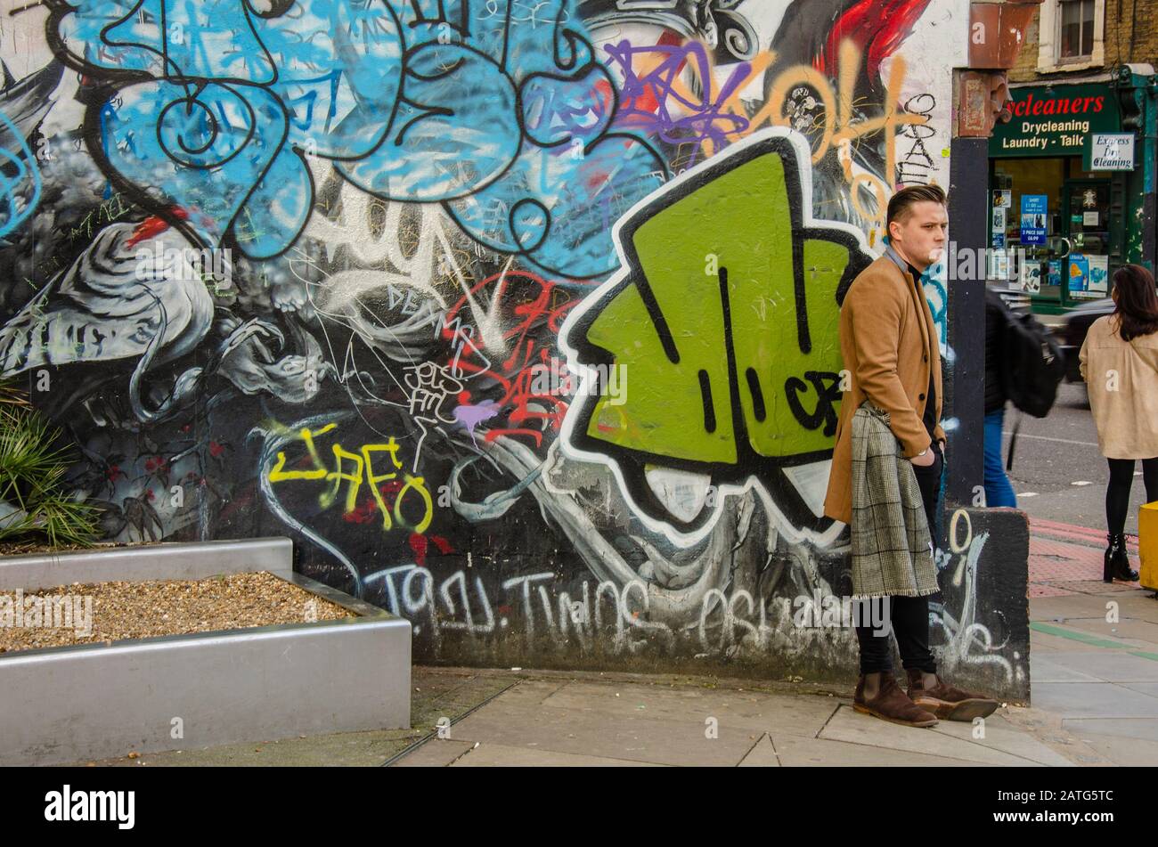 Un uomo si trova su un angolo della strada di fronte a opere d'arte colorate e graffiti. Foto Stock