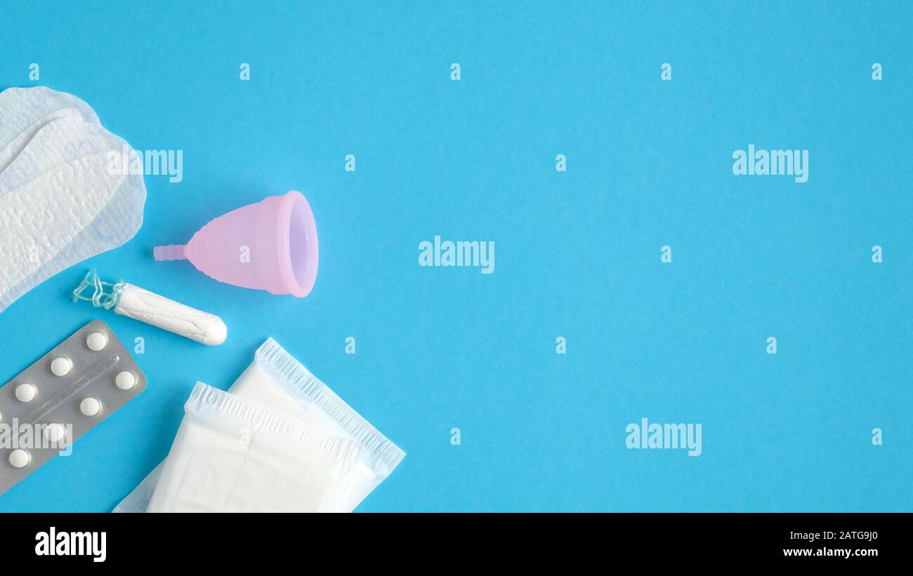 Set di prodotti per l'igiene mestruale su sfondo blu con spazio di copia. Vista dall'alto bicchiere mestruale riutilizzabile, assorbenti igienici, tampone, compresse mediche. Uomo Foto Stock