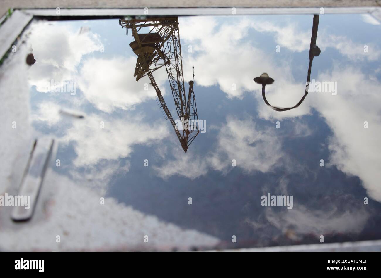 Riflessione urbana: Un palo di illuminazione, una gru e un cielo con nuvole riflesse sulla superficie dell'acqua in un pozza, a Puerto Madero, Buenos Aires, Ar Foto Stock