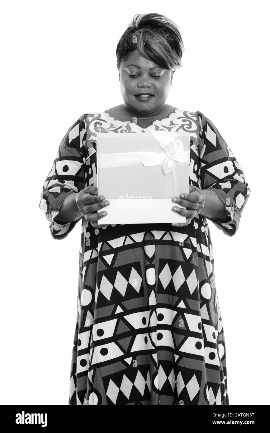 Studio scatto di felice donna africana sovrappeso sorridente e in piedi mentre apre scatola regalo Foto Stock