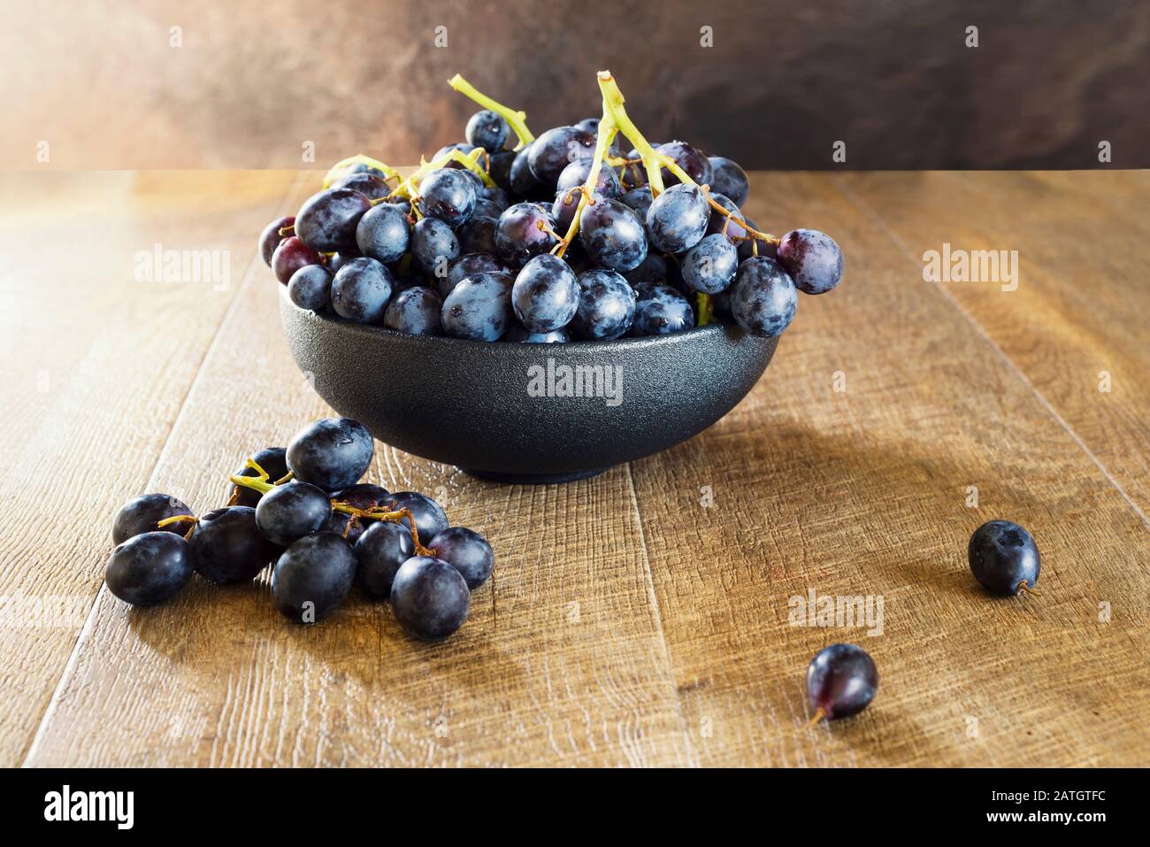 Grappolo di uva nera in una ciotola su fondo di legno. Atmosfera calda. Orientamento orizzontale. Foto Stock