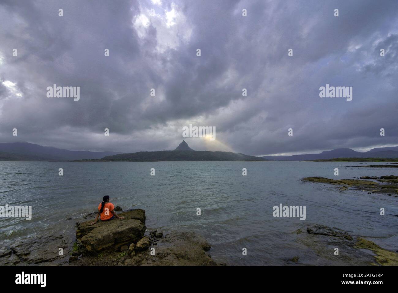 Donna seduta su una roccia al mare con forte tung in primo piano Foto Stock