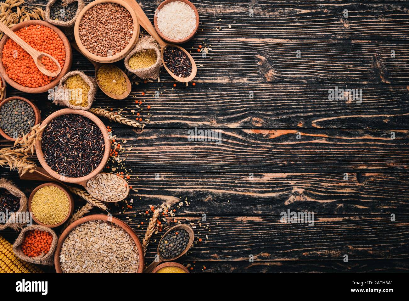 Set di Groats e Grains. Grano saraceno, lenticchie, riso, miglio, orzo, mais, riso nero. Su uno sfondo di legno. Vista dall'alto. Spazio di copia. Foto Stock