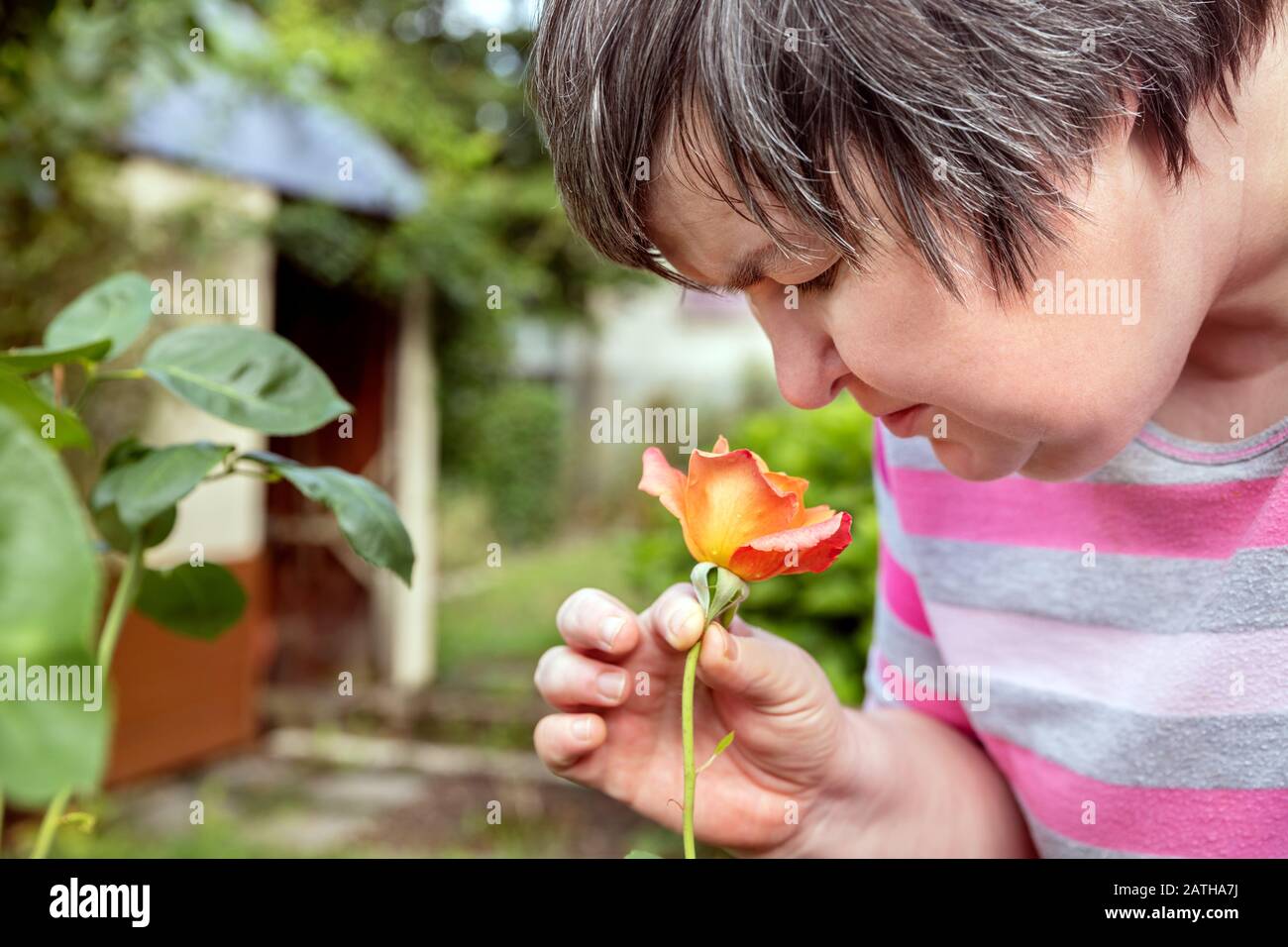 la donna con disabilità mentale sta odorando su una rosa all'aperto nel giardino Foto Stock
