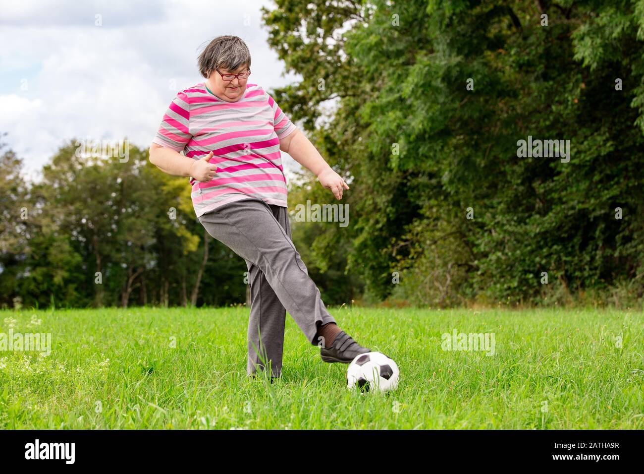 la donna con disabilità mentale sta giocando a calcio per addestrare le sue abilità motorie, divertenti esercizi all'aperto su un prato Foto Stock