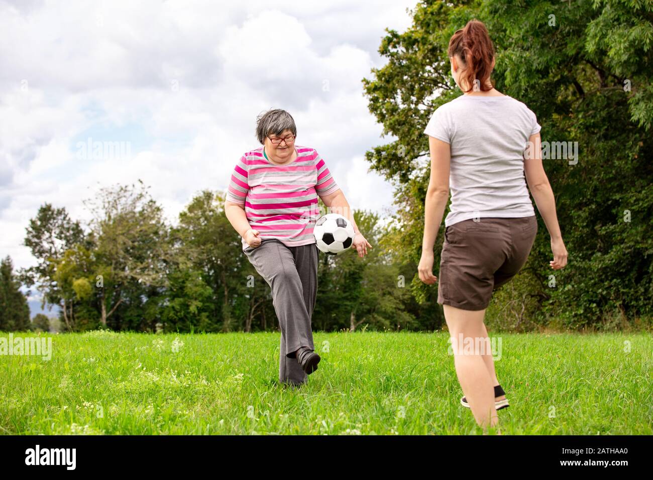 la donna mentale disabile sta giocando a calcio per addestrare le sue abilità motorie, gli esercizi con un amico o terapeuta all'aperto su un prato Foto Stock