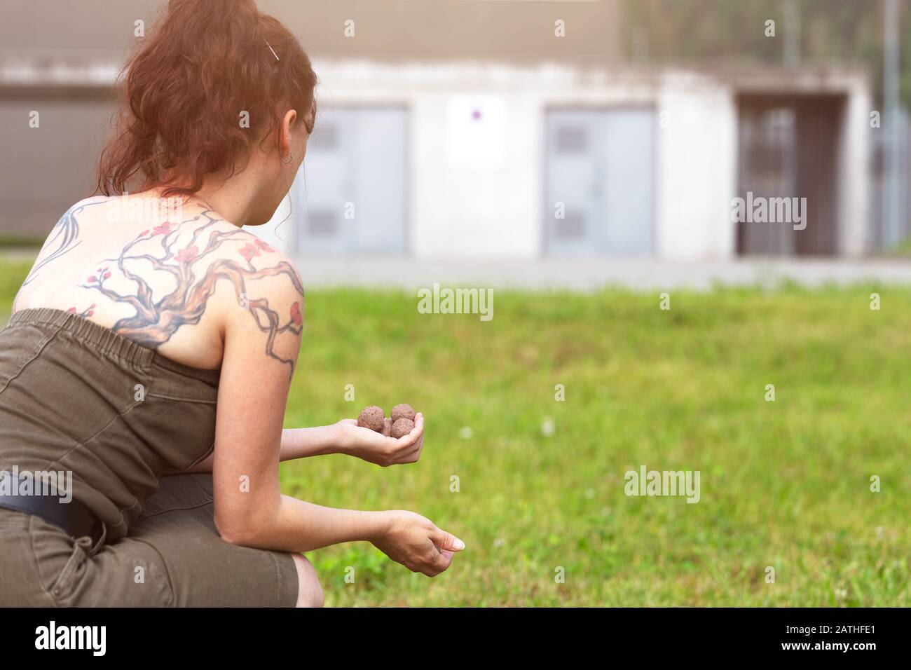 la donna sta tenendo e lanciando palle di seme o bombe di seme di fronte a un brutto edificio grigio, concetto di guerilla giardinaggio Foto Stock