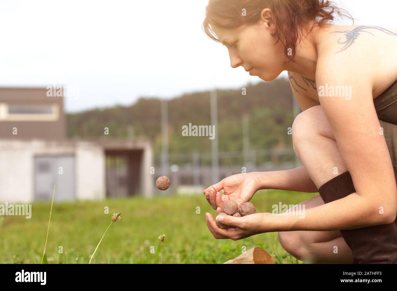 la donna sta tenendo e lanciando palle di seme o bombe di seme di fronte a un brutto edificio grigio, concetto di guerilla giardinaggio Foto Stock