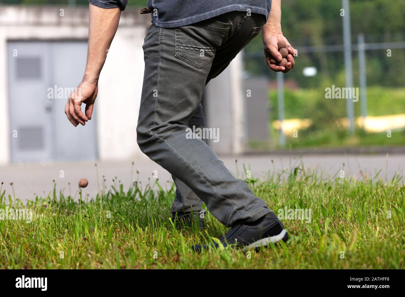 l'uomo sta tenendo e gettando le sfere di seme o le bombe di seme davanti ad un edificio grigio brutto, concetto di guerilla giardinaggio Foto Stock