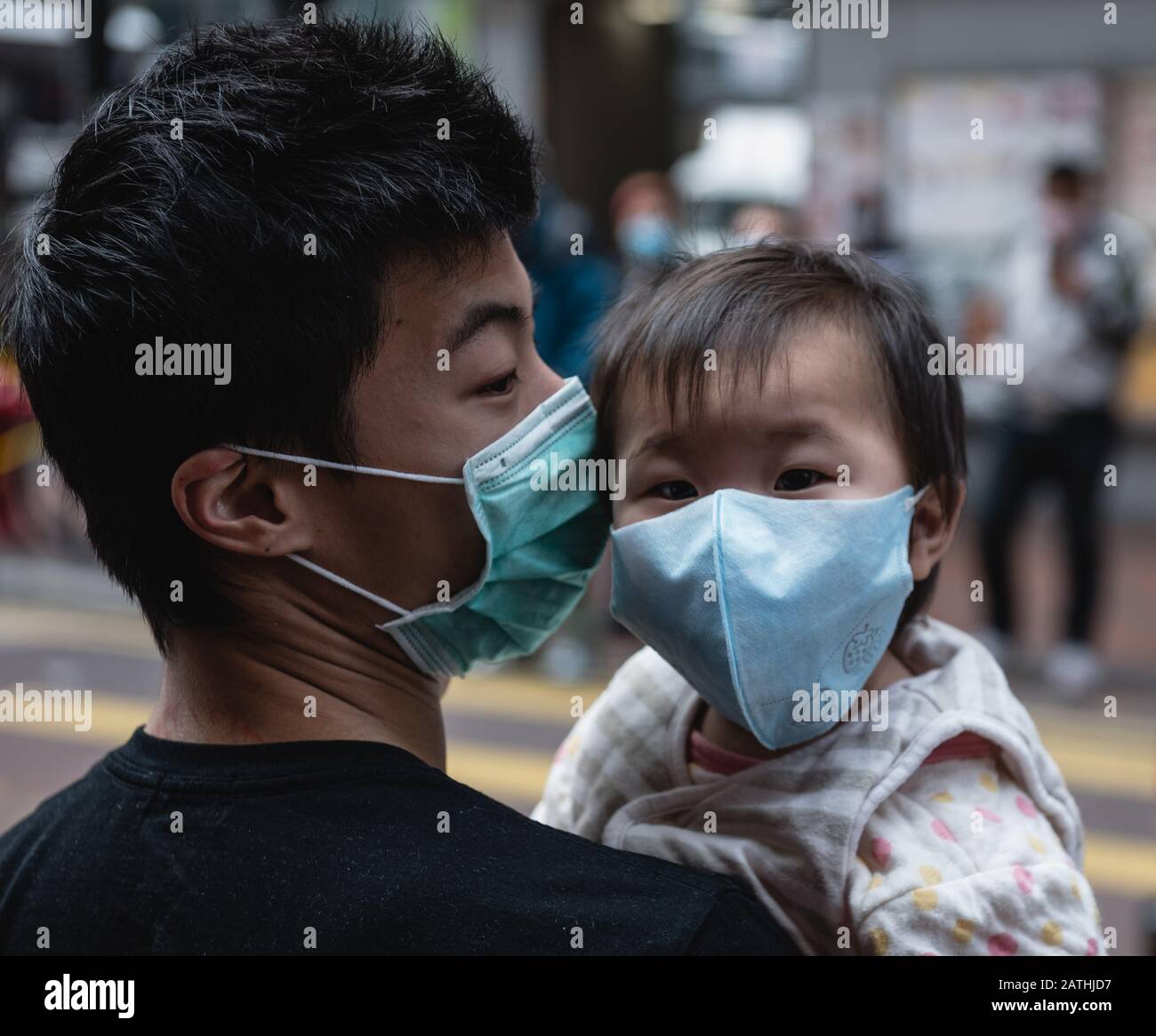 Un bambino piccolo indossa una maschera facciale mentre è trasportato da suo padre.Centinaia dei residenti di Hong Kong allineati per le ore in previsione della consegna della maschera chirurgica ad un deposito locale di reparto. I clienti hanno ricevuto i biglietti per garantire l'acquisto delle maschere. Foto Stock