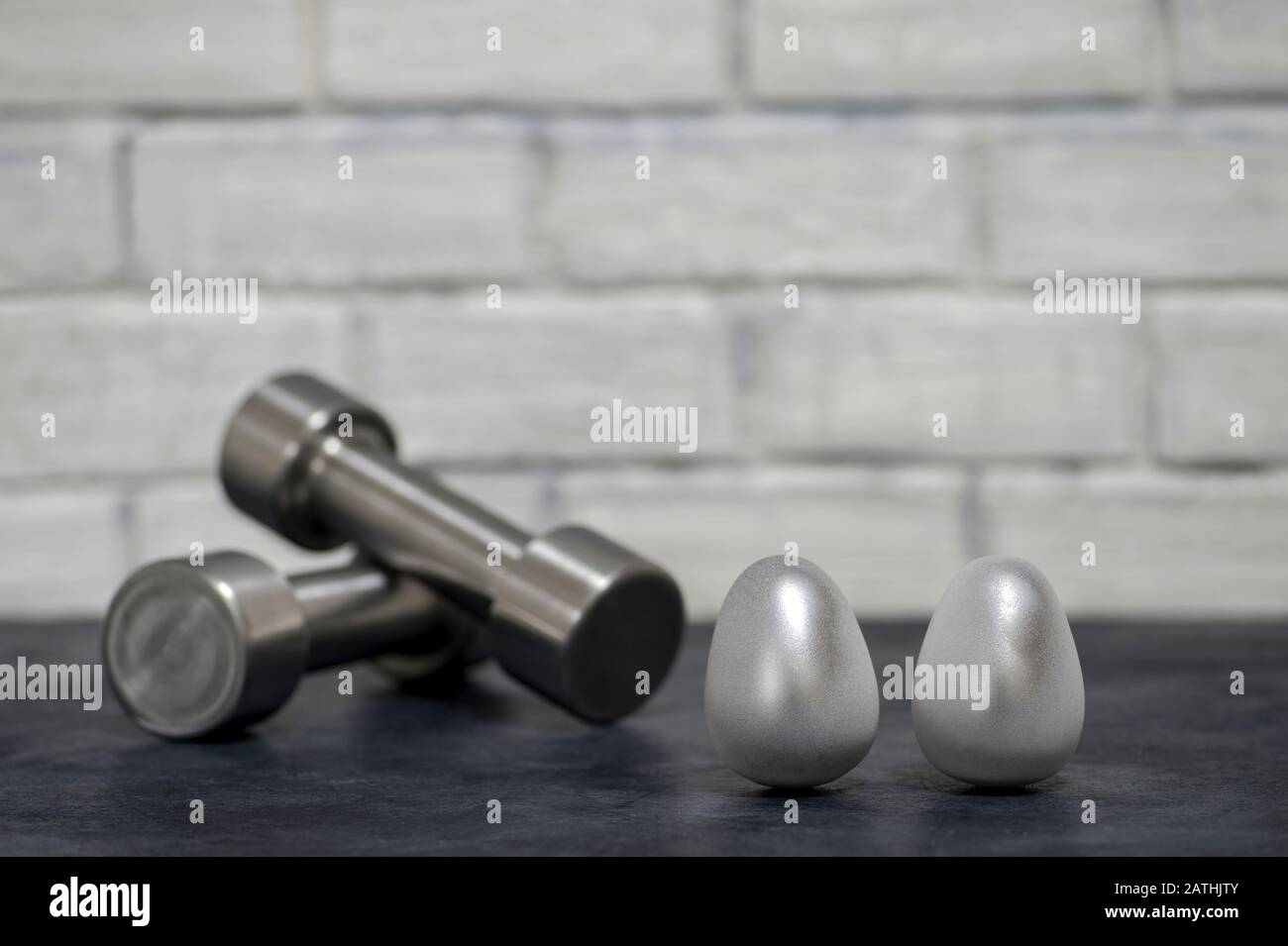 Manubri metallici e uova d'acciaio contro un muro di mattoni bianchi. Il concetto di perseveranza ed efficienza sopra lei. Foto Stock