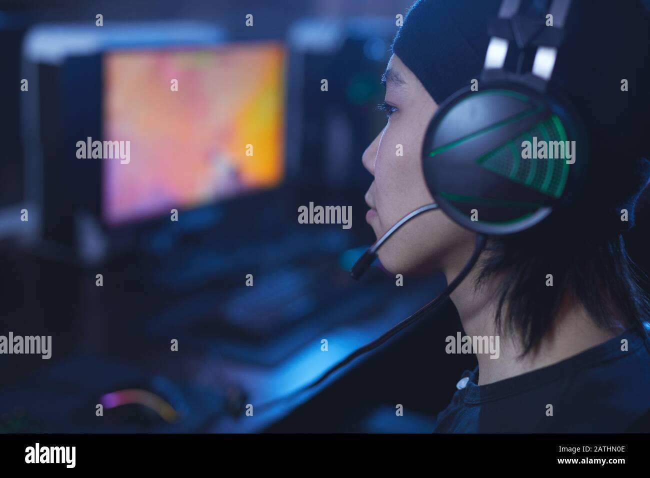 Vista laterale primo piano di giovani asiatici che giocano videogiochi e indossano cuffie in buio cyber come interni, copia spazio Foto Stock
