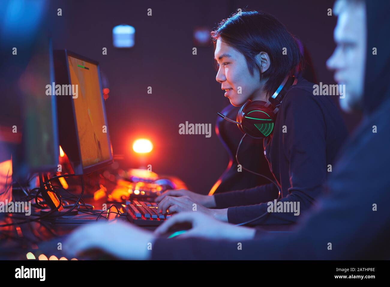 Vista laterale ritratto di uomo asiatico sorridente che gioca video giochi con pro cyber sport team, copia spazio Foto Stock