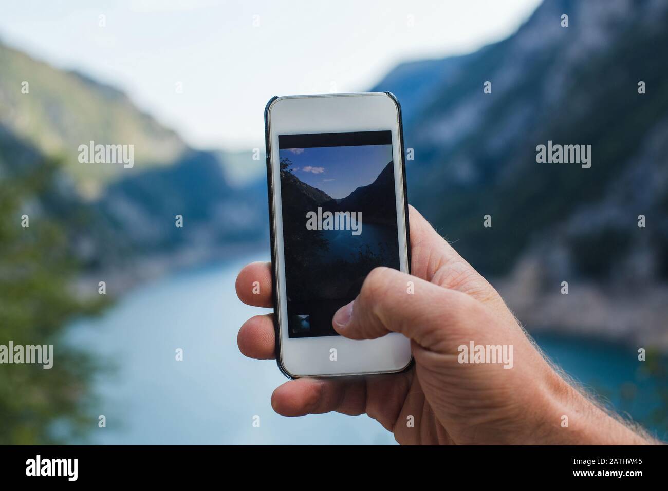 Un uomo scatta una foto del paesaggio di montagna al telefono mentre la tiene in una mano Foto Stock