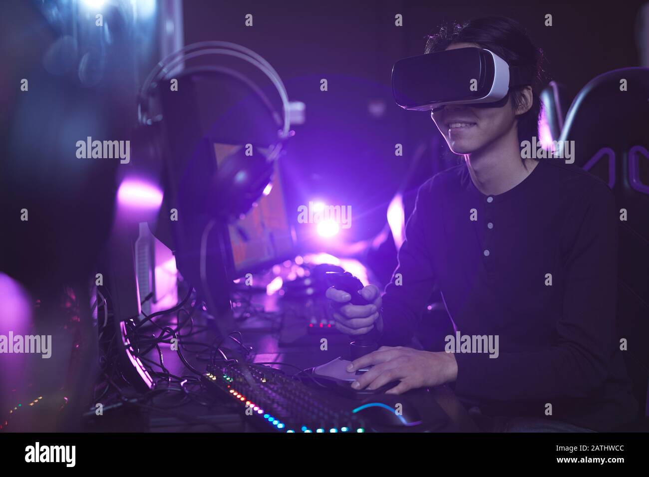 Ritratto della vista laterale di un giovane asiatico che indossa un visore VR mentre gioca ai videogame utilizzando il cambio di corsa in interni informatici scuri, copia spazio Foto Stock