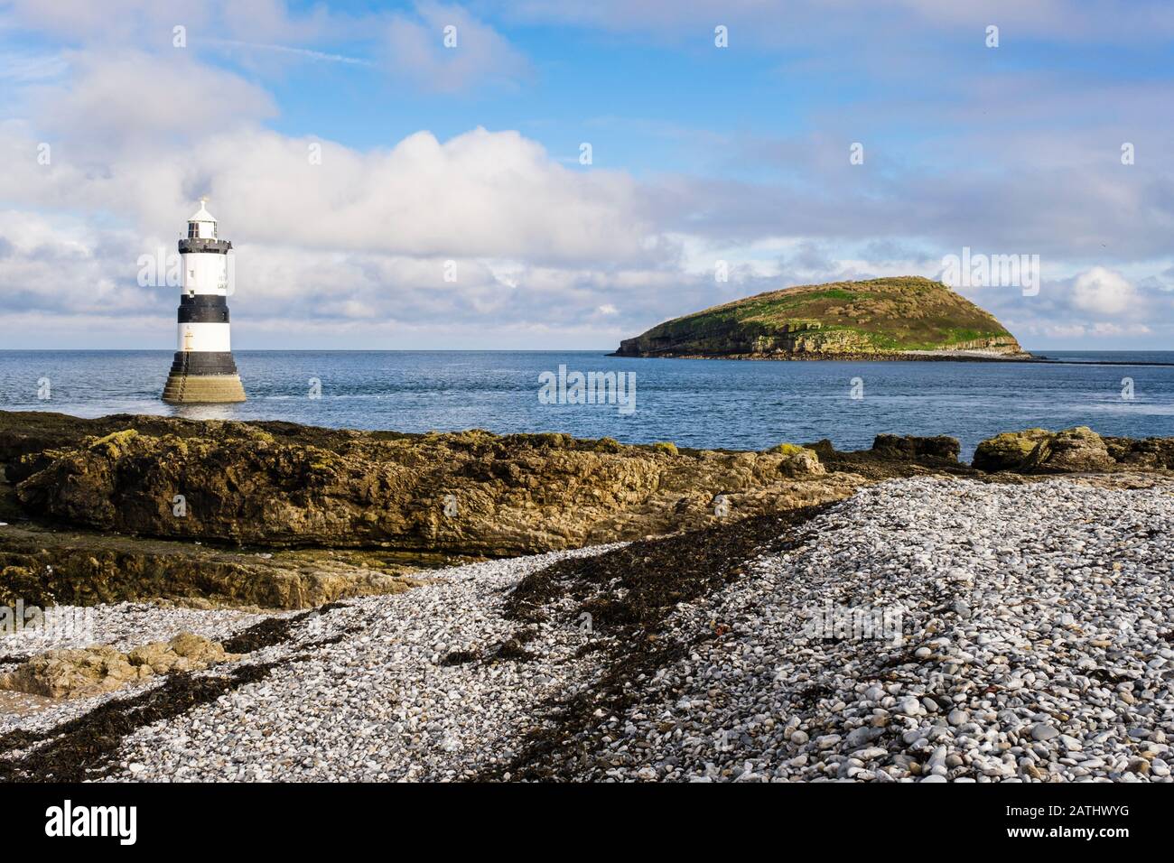 Faro di Penmon e Puffin Island (Ynys Seiriol) da spiaggia di ciottoli a Penmon Point (Trwyn Du), Isola di Anglesey, Galles, Regno Unito, Gran Bretagna Foto Stock