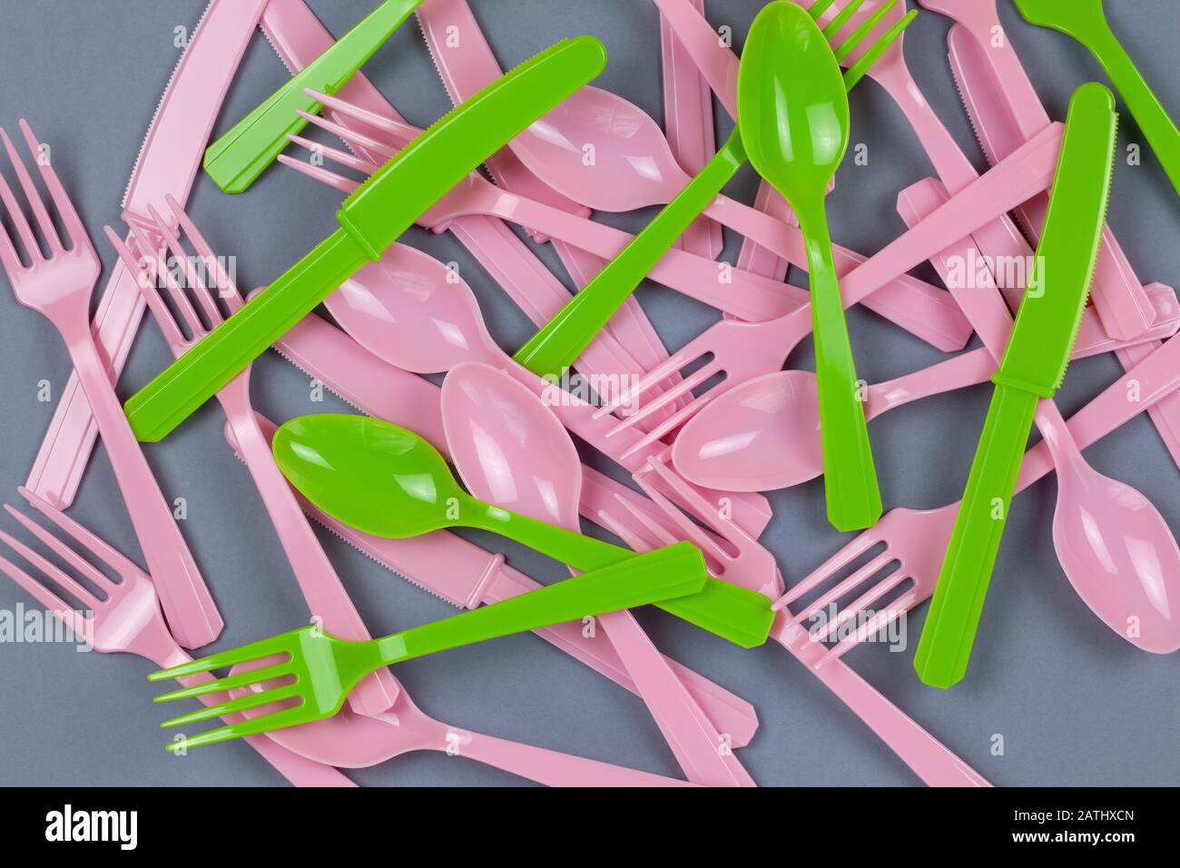 Sfondo da biforchette, cucchiai, coltelli riciclabili rosa e verde, realizzati con amido di mais su carta grigia. Eco, zero rifiuti, alternativa alla plastica Foto Stock