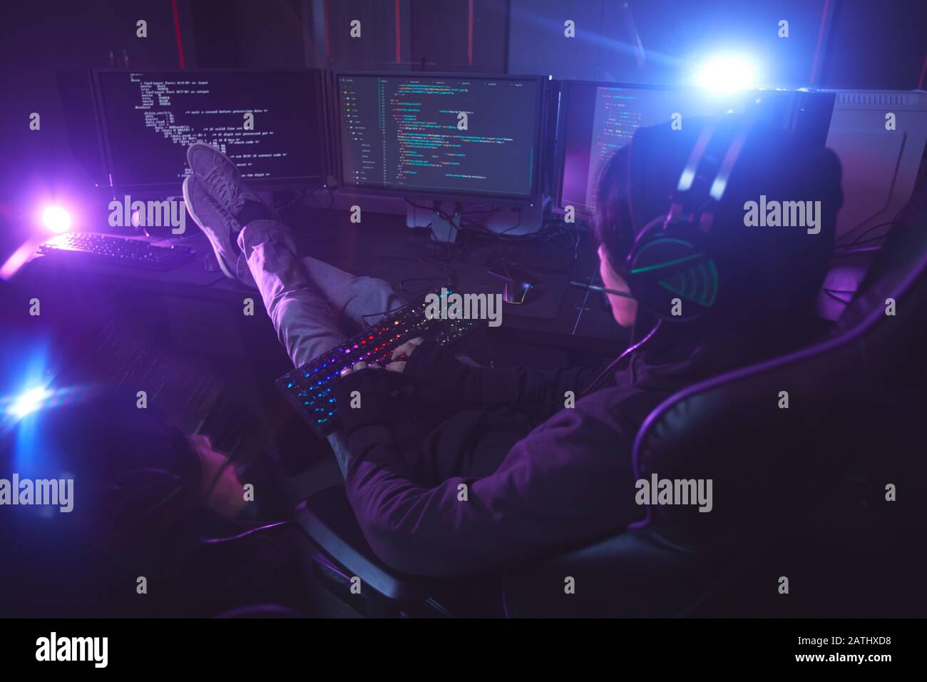 Vista posteriore al giovane uomo circondato da più schermi programmazione o hacking sicurezza in camera oscura, copia spazio Foto Stock